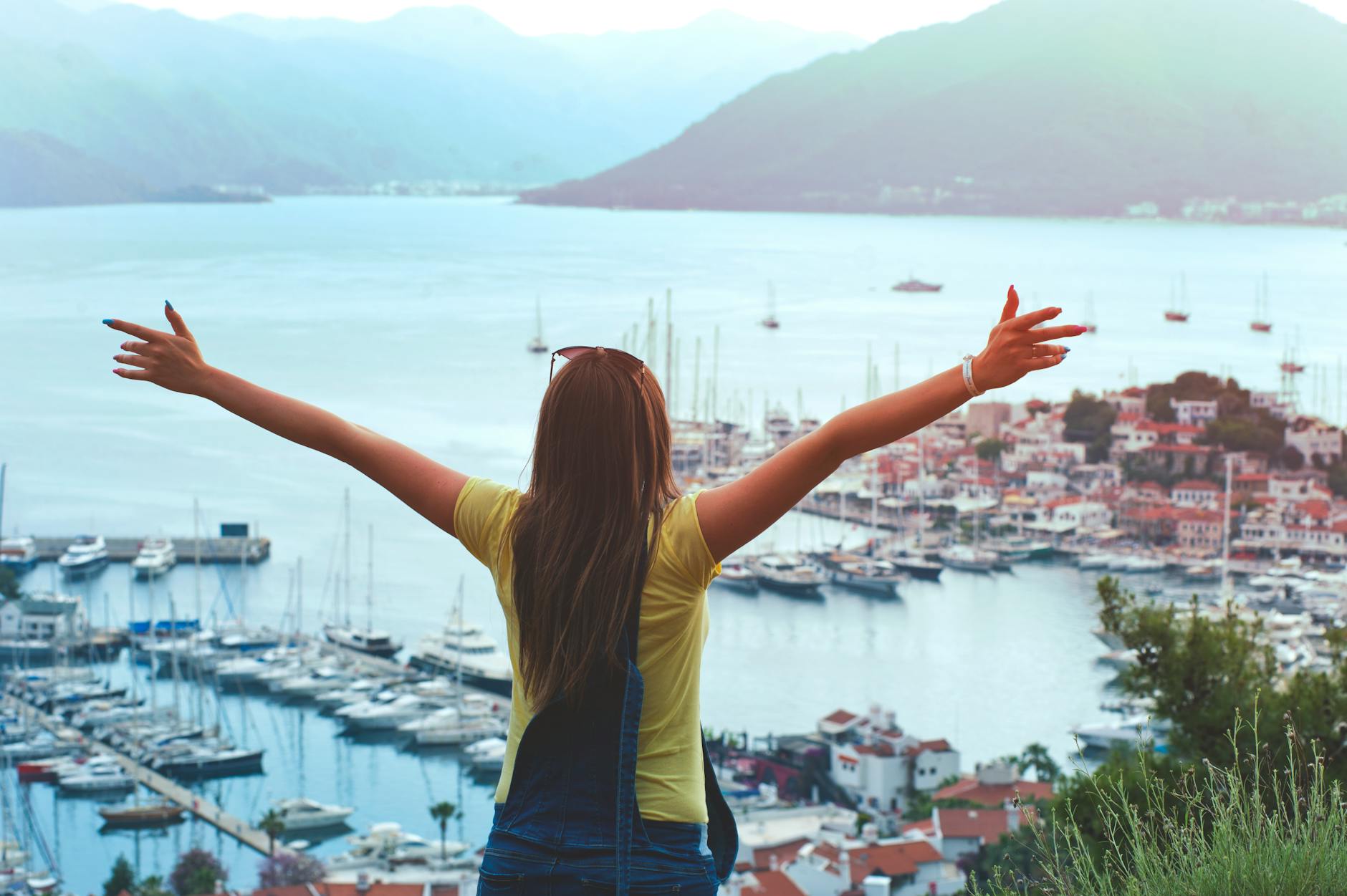 woman raising her hands facing cityscape near body of water