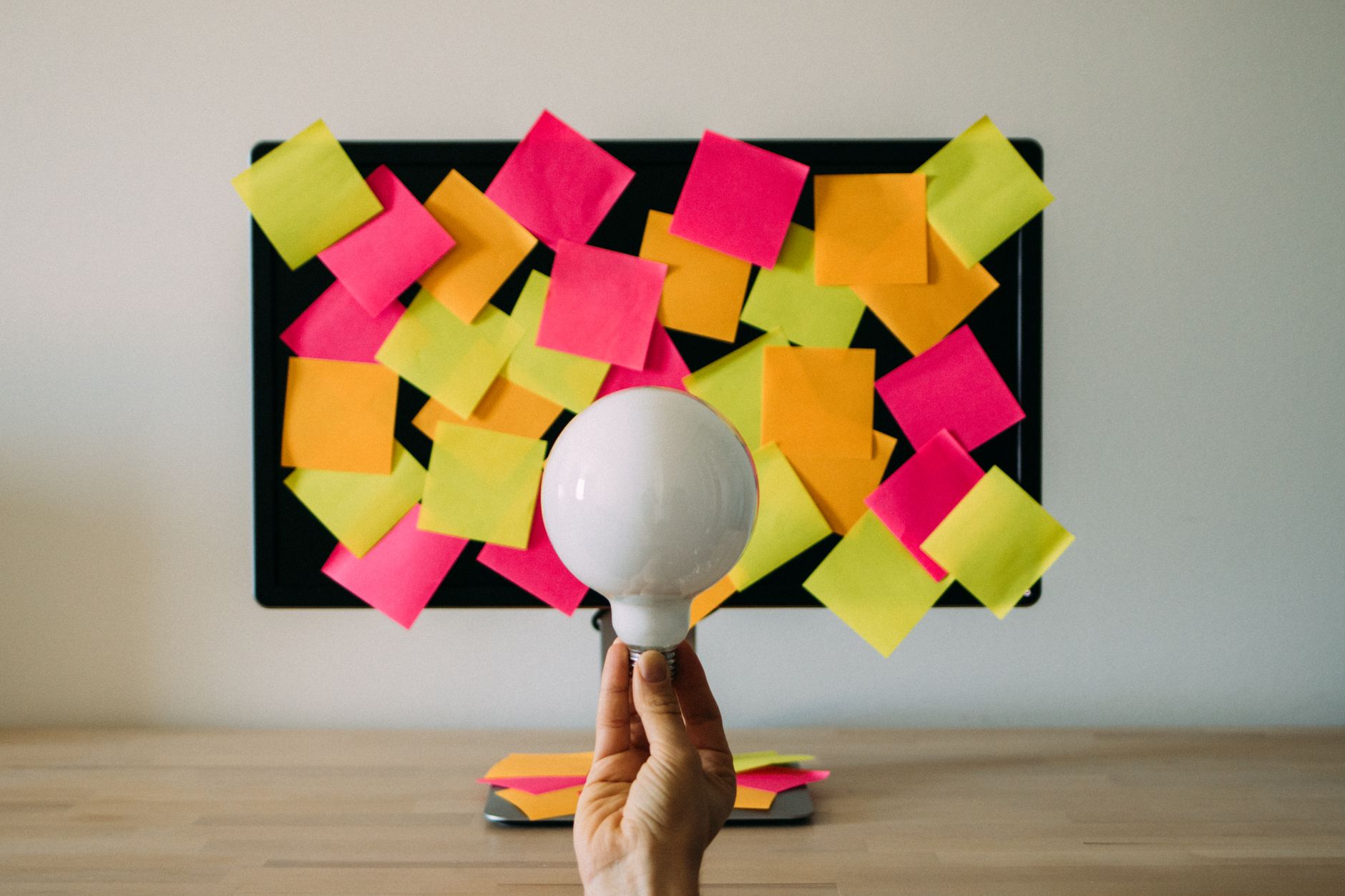 hand holding a light bulb against a board with sticky notes