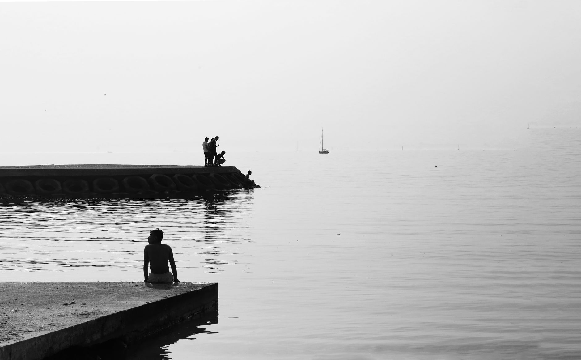 person sitting on concrete dock in grayscale photography