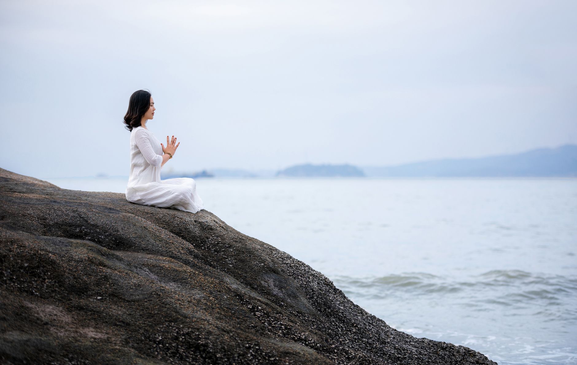 woman in white dress meditating on coast