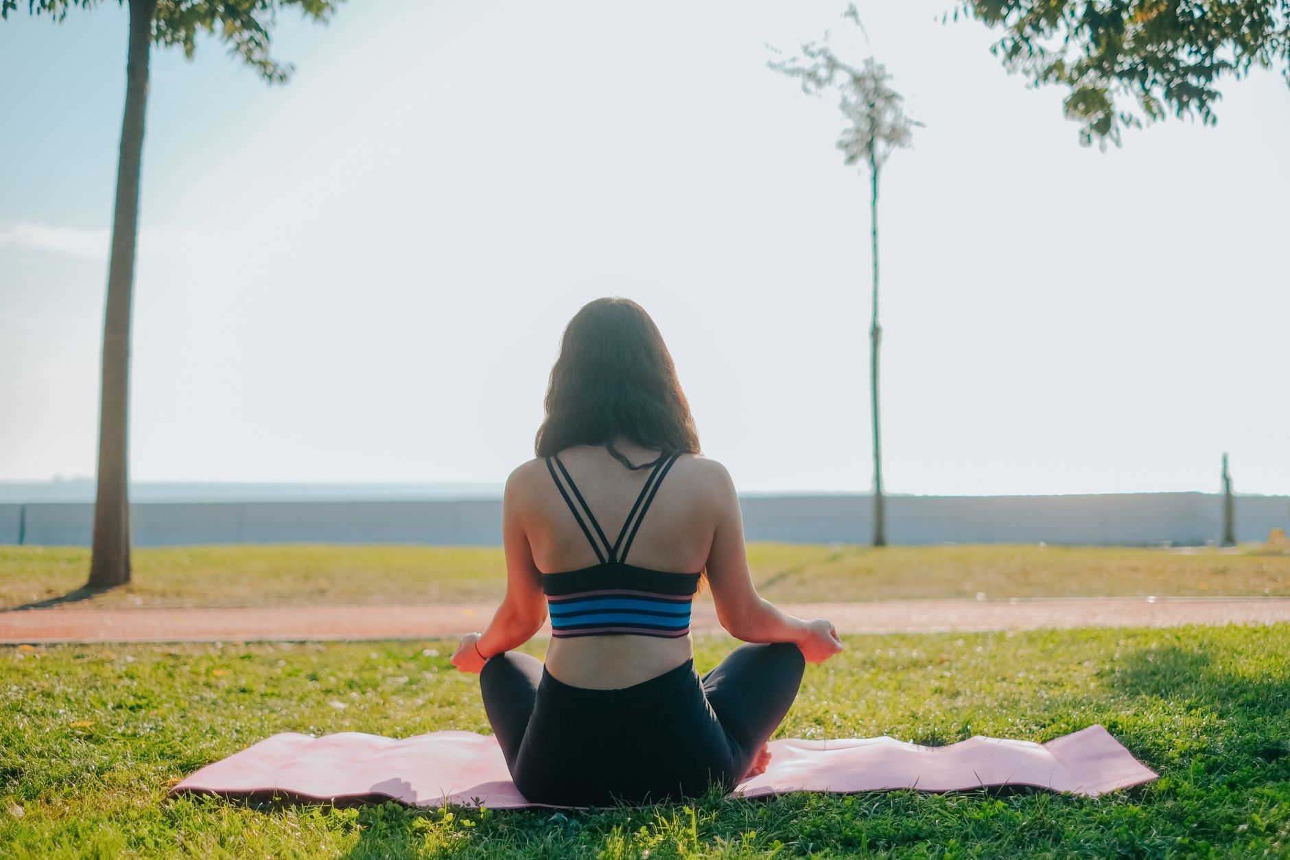 a back view of a woman meditating at the park