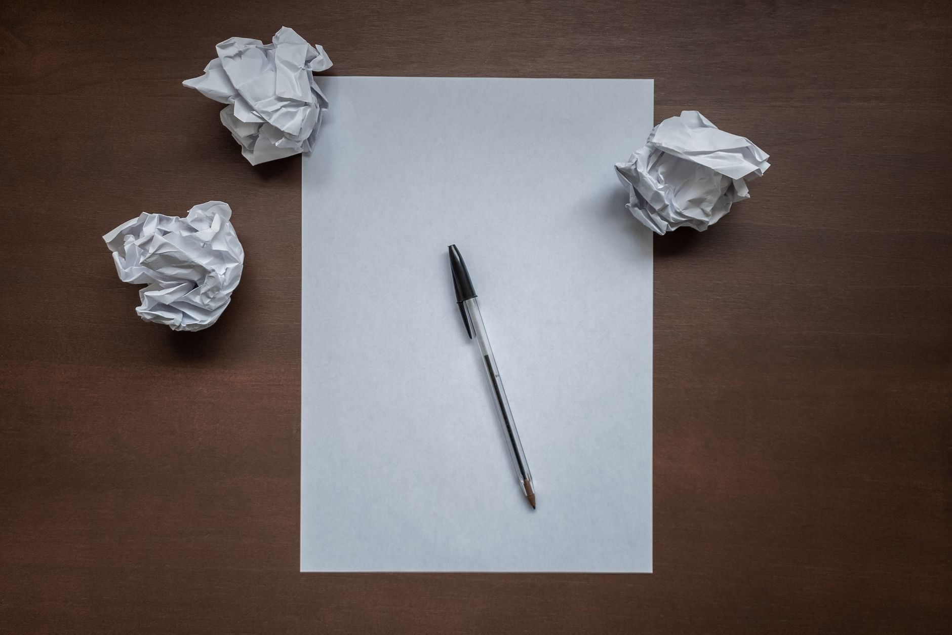 flat lay with blank writing sheet pen and crumpled paper balls on top of wooden office desk writer s block or creativity crisis concept top down view