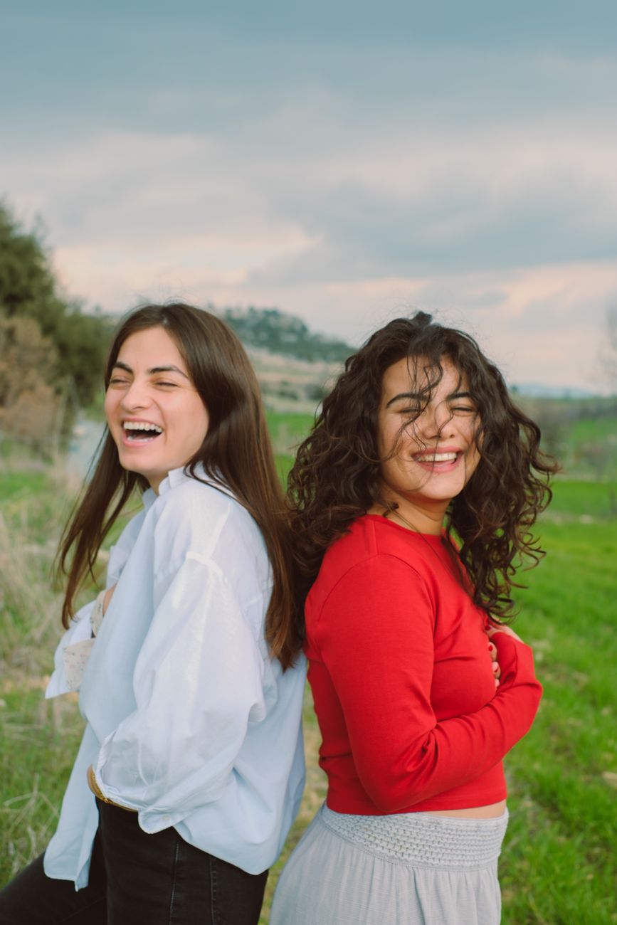 laughing young women standing back to back on a meadow