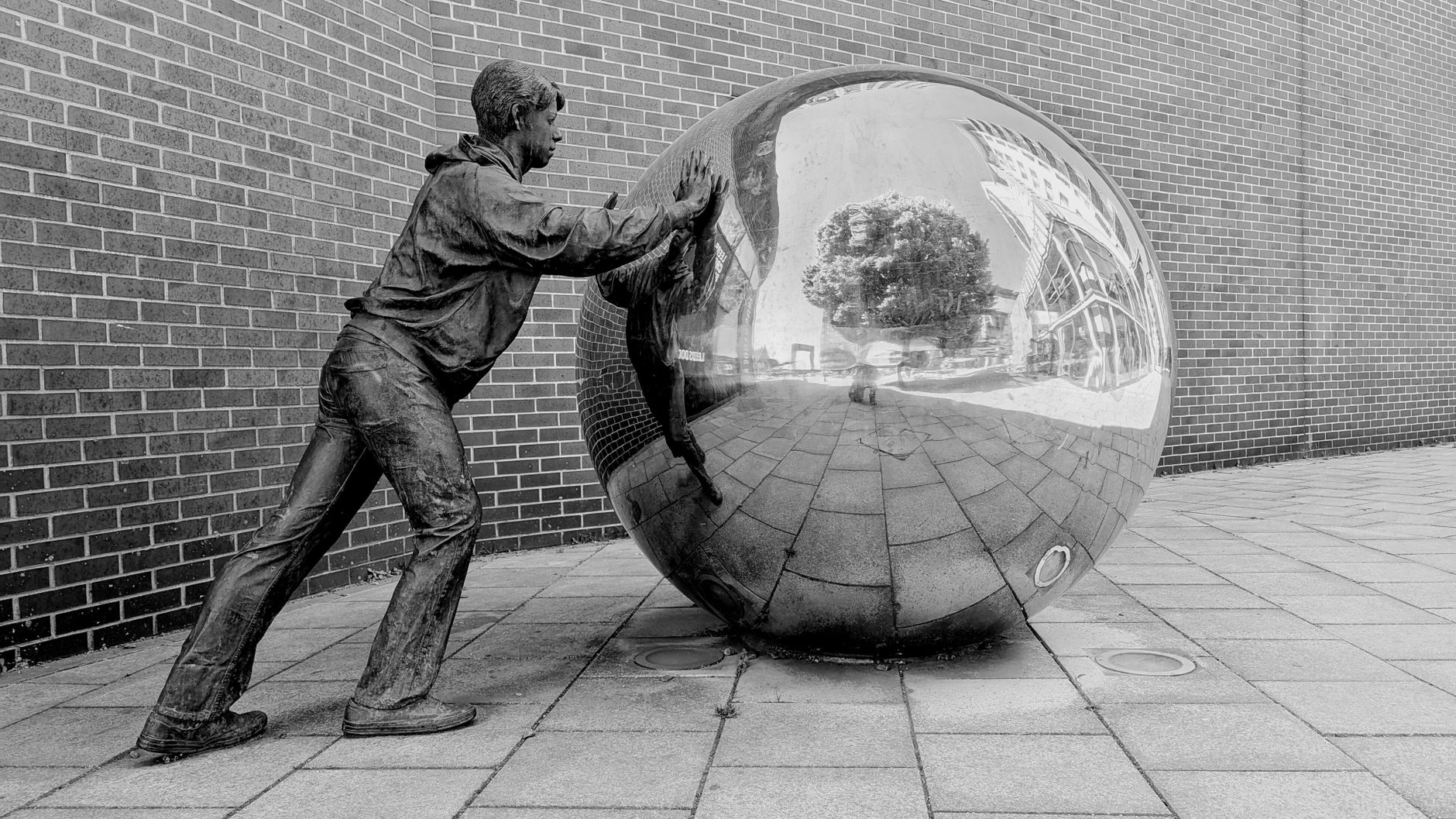 monochrome sculpture of man pushing reflective sphere