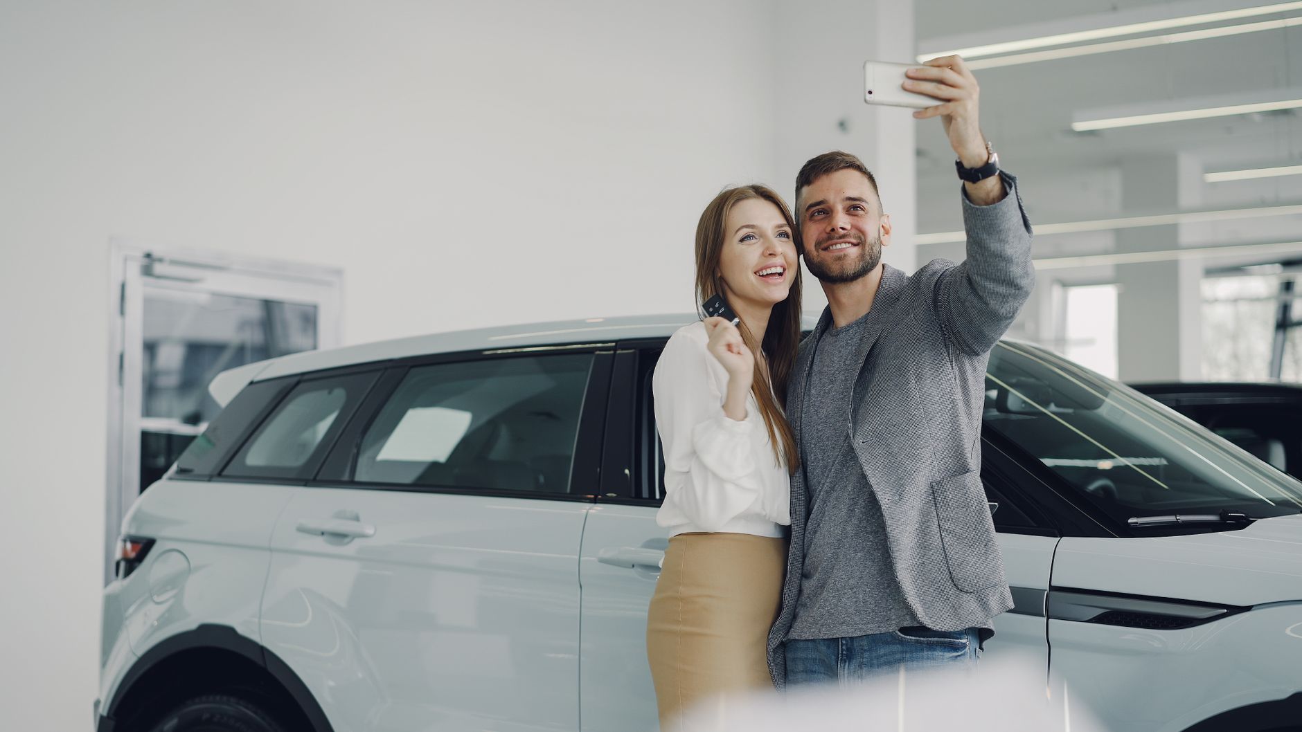 happy couple taking selfie with new car in showroom