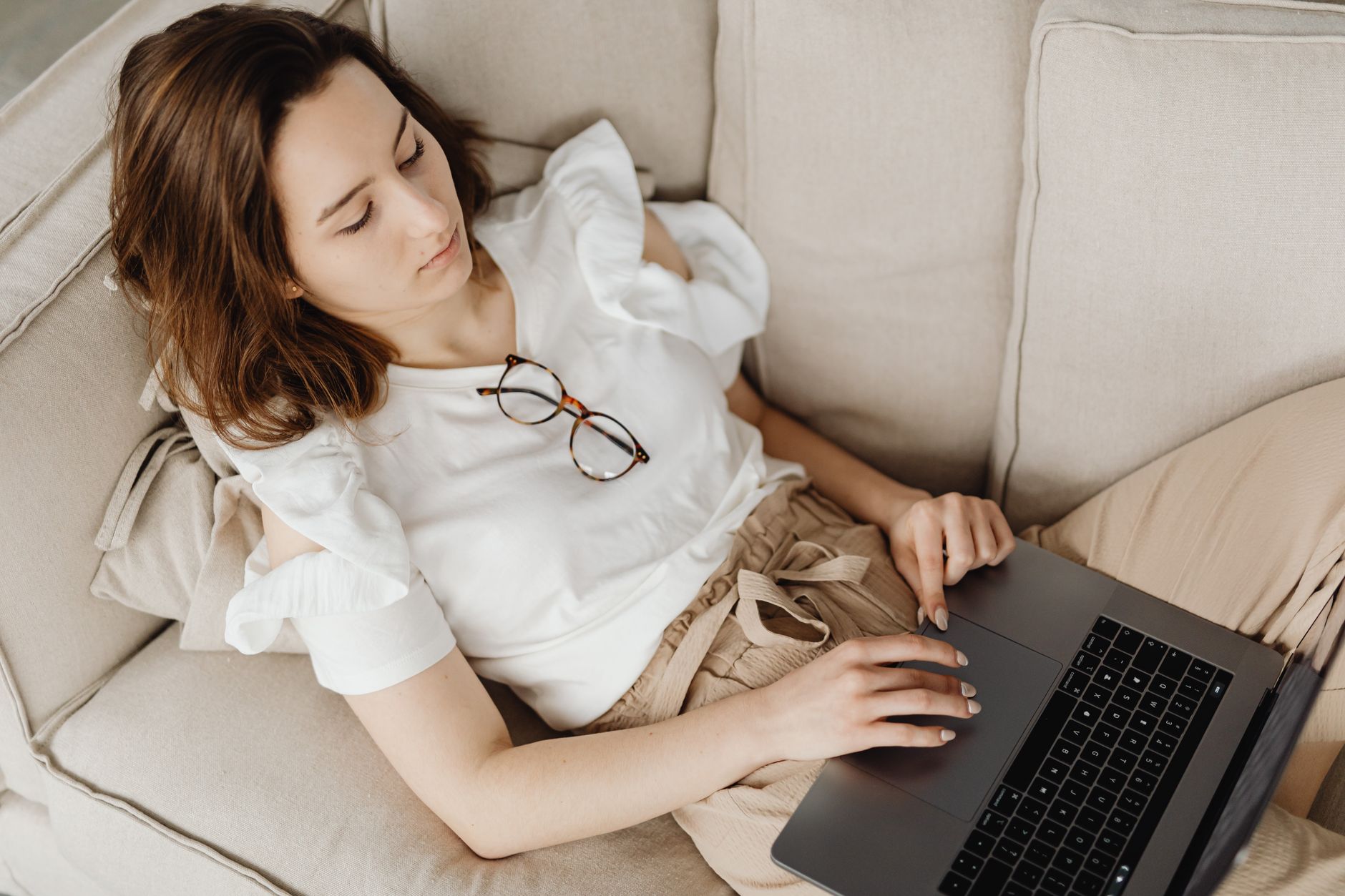 a woman browsing a laptop while lying on the couch